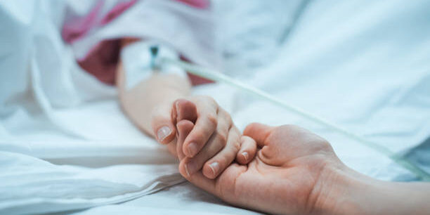 Recovering Little Child Lying in the Hospital Bed Sleeping, Mother Holds Her Hand Comforting. Focus on the Hands. Emotional Family Moment.