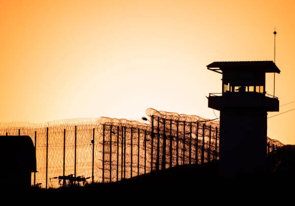 Silhouette of barbed wires and watchtower of prison.