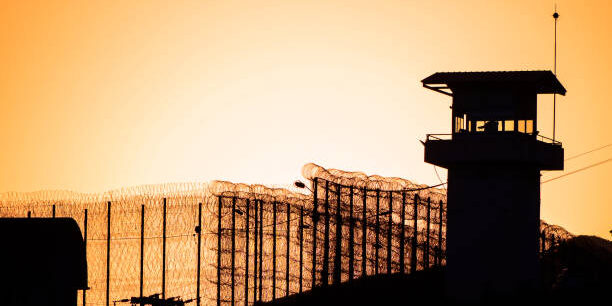 Silhouette of barbed wires and watchtower of prison.